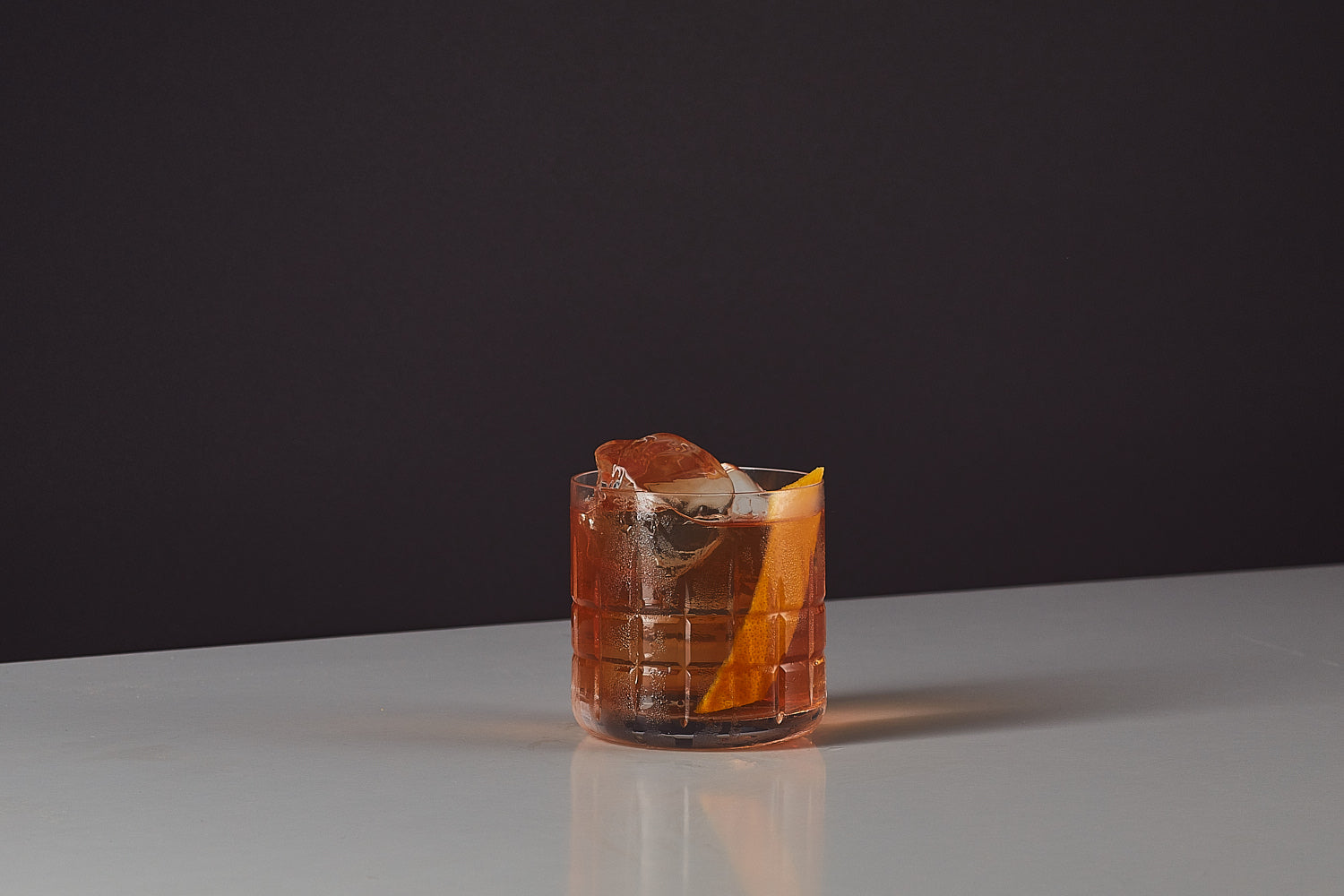 Image of an Old Fashioned original recipe premixed ready to drink whiskey cocktail from Craft Cocktails in a tumbler glass with ice and an orange peel garnish shot on a black and grey background