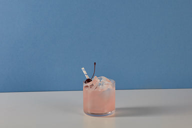 Image of an Aviation gin original recipe premixed ready to drink cocktail from Craft Cocktails in a tumbler glass with ice, blue and white stripy straw, and maraschino cherry garnish shot on a blue and white background