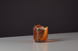 Image of an Old Fashioned original recipe premixed ready to drink whiskey cocktail from Craft Cocktails in a tumbler glass with ice and an orange peel garnish shot on a black and grey background