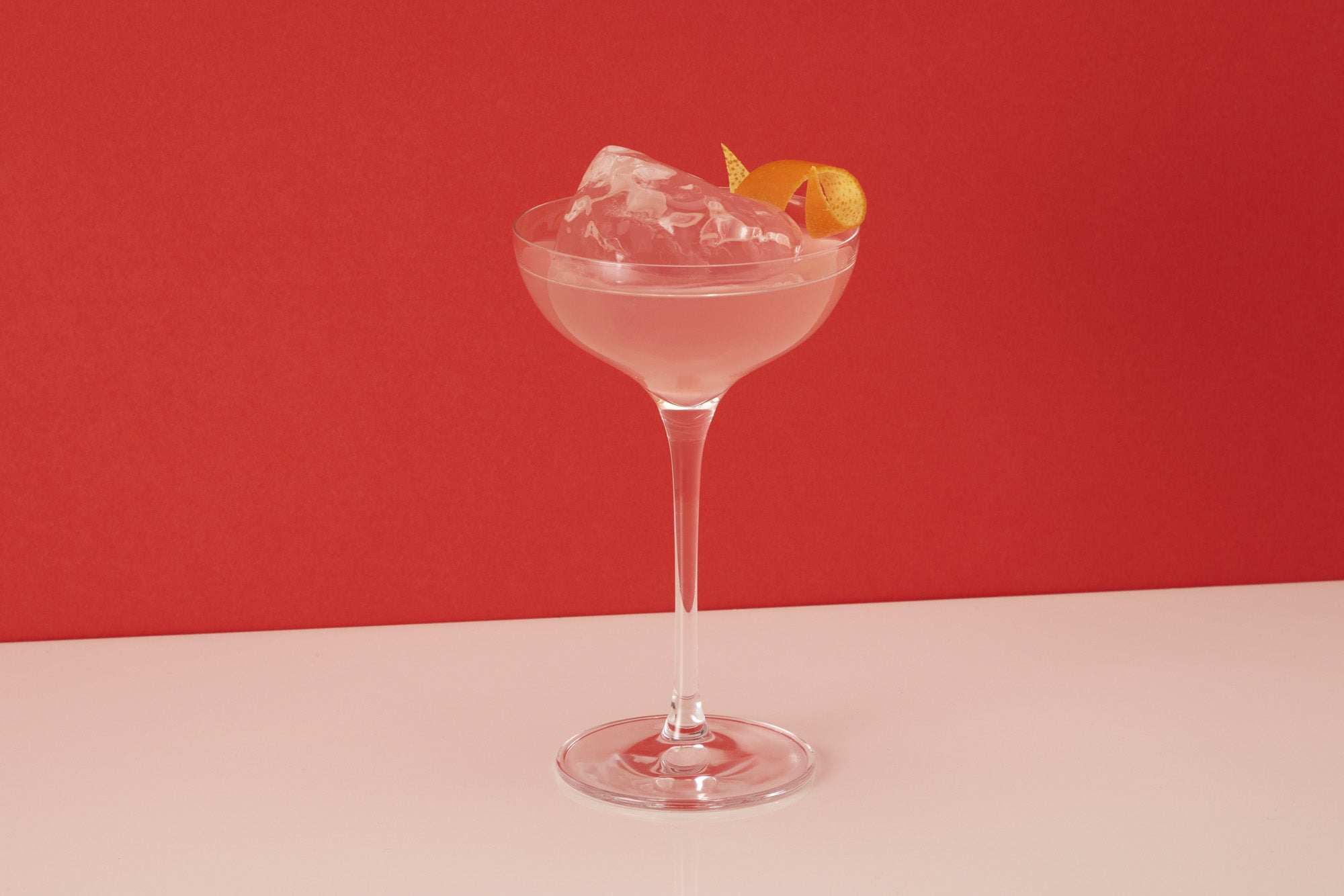 Image of an Cosmopolitan vodka original recipe premixed ready to drink cocktail from Craft Cocktails in a martini glass with ice and an orange peel garnish shot on a red and white background